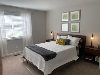 A bedroom with a large bed and a window with blinds.